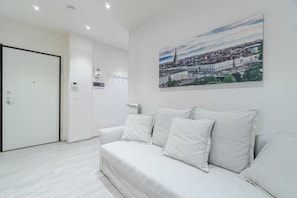 A modern hotel room with a white sofa, a cityscape painting on the wall, and a door to the left. - Cozy and bright apartment located in a prestigious area of the city near the Polytechnic, located less than 2 km from the flat, and well connected to the historic center thanks to public transport that allows you to reach all the points of interest in th (Torino)