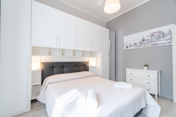 A modern bedroom with a bed, bedside tables, a headboard, a nightstand, a wall-mounted lamp, and a painting.