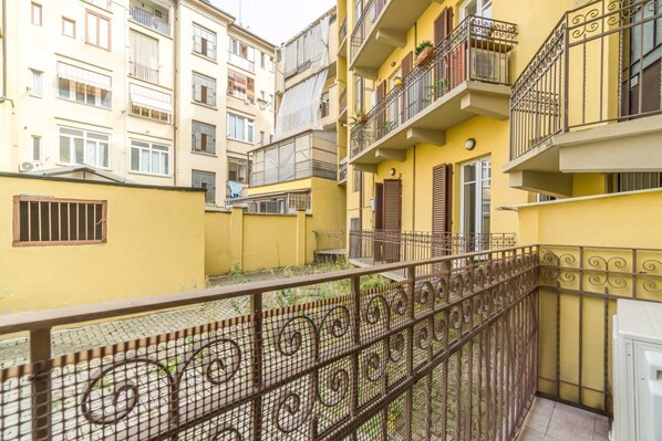 A multi-story residential building with balconies, a gated courtyard, and a metal fence.