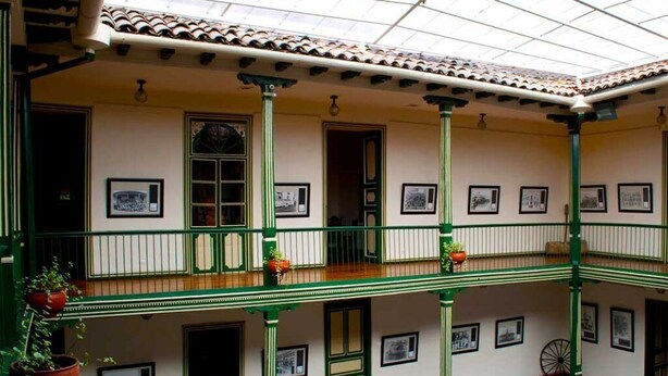 A covered courtyard with a tiled roof, green railings, and multiple framed pictures on the walls. - JOMALEY REAL HOTEL (Loja)