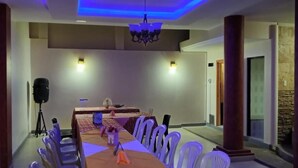 A conference room with a long table, white chairs, a chandelier, and a speaker on a tripod. - JOMALEY REAL HOTEL (Loja)