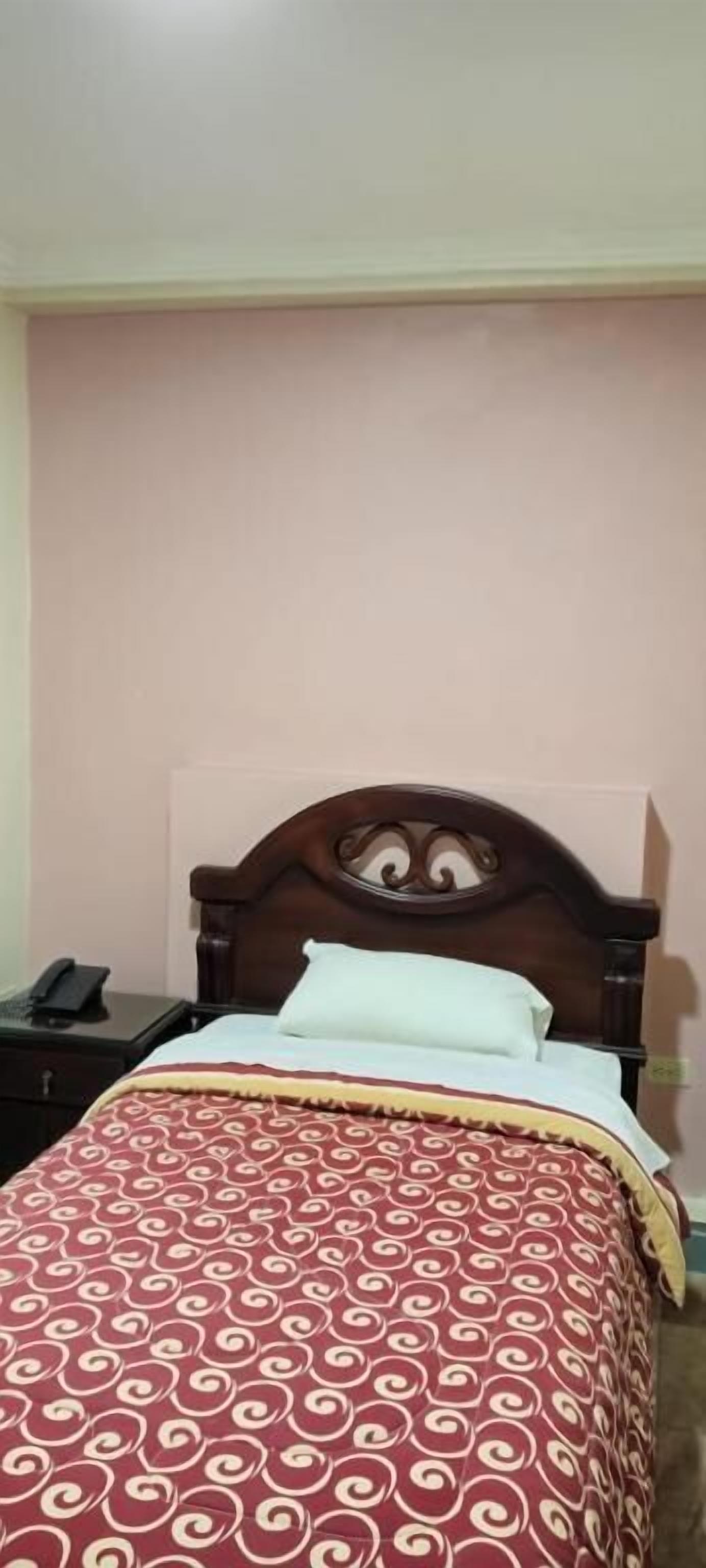 Uma cama de solteiro com cabeceira de madeira, colcha estampada e mesa de cabeceira com telefone.
