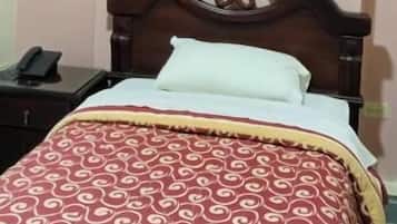 Uma cama de solteiro com cabeceira de madeira, colcha estampada e mesa de cabeceira com telefone.