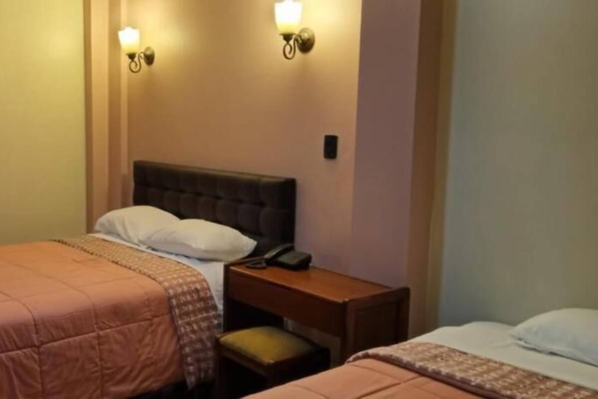 A hotel room with two beds, each with a headboard and bedside tables.
