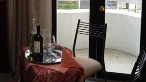A hotel room with a bed, a table with a tray of wine, and a view of the city through a large window. - JOMALEY REAL HOTEL (Loja)