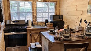 A cozy kitchen with wooden walls and a central island, equipped with a stove, microwave, and various kitchen utensils.
