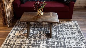 A cozy cabin interior with a wooden wall, a red sofa, a wooden coffee table, and a patterned rug.