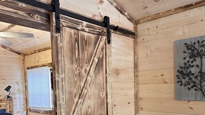 A wooden cabin interior with a bed, a sofa, and a sliding barn door.