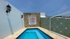 Una piscina rectangular con borde de piedra, un muro de piedra con un escudo y una cerca con diseño.