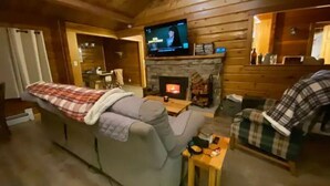 Interior acogedor de una cabaña de madera con sofá, una mesita, televisor y chimenea.