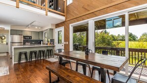 A spacious kitchen with a central island, a dining area with a large wooden table, and a balcony with a view of greenery. - Fox Wood Path l HOT TUB l A&D Rise Getaways (Galena)