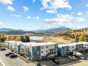 Un hotel de varios pisos con estacionamiento, un lago y montañas al fondo.
