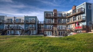 A modern multi-story residential building with balconies, a grassy lawn, and a clear sky. - Lakeside One-Bedroom with Balcony/Views! Close to Keystone.  (Dillon)