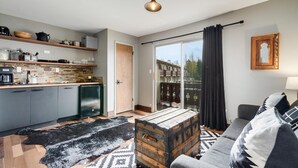 A modern apartment with a kitchen, a living area with a sofa and a coffee table, a sliding glass door to a balcony, and a view of the city. - Lakeside One-Bedroom with Balcony/Views! Close to Keystone.  (Dillon)