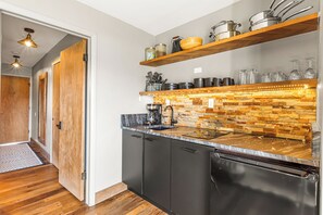A modern kitchen with a stone backsplash, wooden shelves, and a black dishwasher.