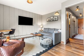 Una sala de estar moderna con un sofá gris, un televisor de pantalla plana, una mesa de centro y un sillón de cuero.