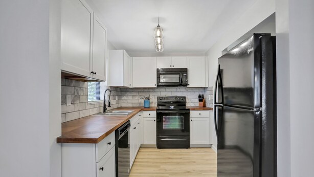 Een moderne keuken met witte kasten, een zwarte koelkast, een magnetron en een houten aanrecht.