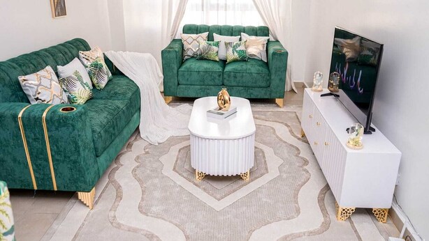 Una sala de estar con dos sofás verdes, una mesa de centro blanca y un televisor sobre un mueble blanco.