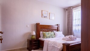Un dormitorio ordenado con una cama de madera, una mesita de noche con lámpara y una ventana con cortinas.