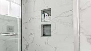 Ein Badezimmer mit Marmorwänden, einer Duschkabine aus Glas und einem Ablagebereich für Pflegeprodukte.