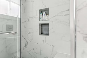 Ein Badezimmer mit Marmorwänden, einer Duschkabine aus Glas und einem Ablagebereich für Pflegeprodukte.