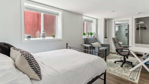 Ein modernes Schlafzimmer mit Bett, Schreibtisch und Stuhl, sowie einem großen Fenster und einem Spiegel.