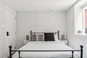 Un dormitorio con una cama, dos mesitas de noche, una ventana y una puerta.