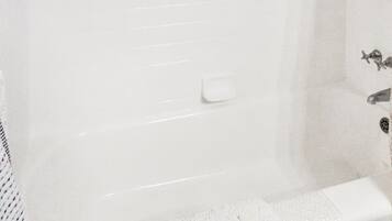 Eine weiße Badewanne mit Duschkopf, einer Seifenschale und einem Handtuch am Rand.