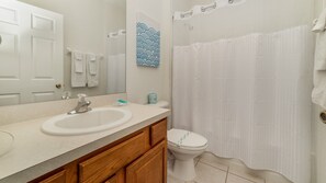 Bathroom features a sink, mirror, and toilet, with a shower area and vanity with drawers.