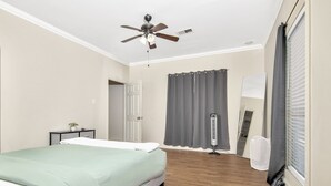 A bedroom with a bed, a ceiling fan, a window with curtains, and a radiator.