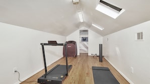 A small, well-lit room with a treadmill, a stationary bike, and a large suitcase.