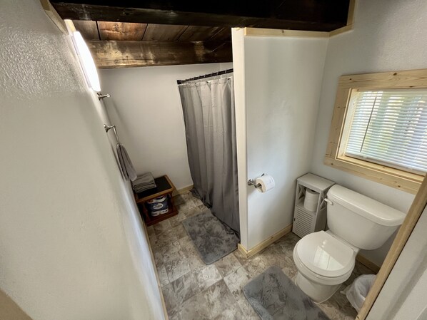 Et lille badeværelse med toilet, bruseforhæng og en hylde med et håndklæde.