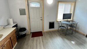 A compact room with a wooden door, a small table with chairs, a television, and a microwave on the counter. - Studio Apartment in Wallace (Wallace)