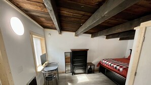 A small, cozy room with a bed, a desk with a chair, a dresser, and a window. - Studio Apartment in Wallace (Wallace)