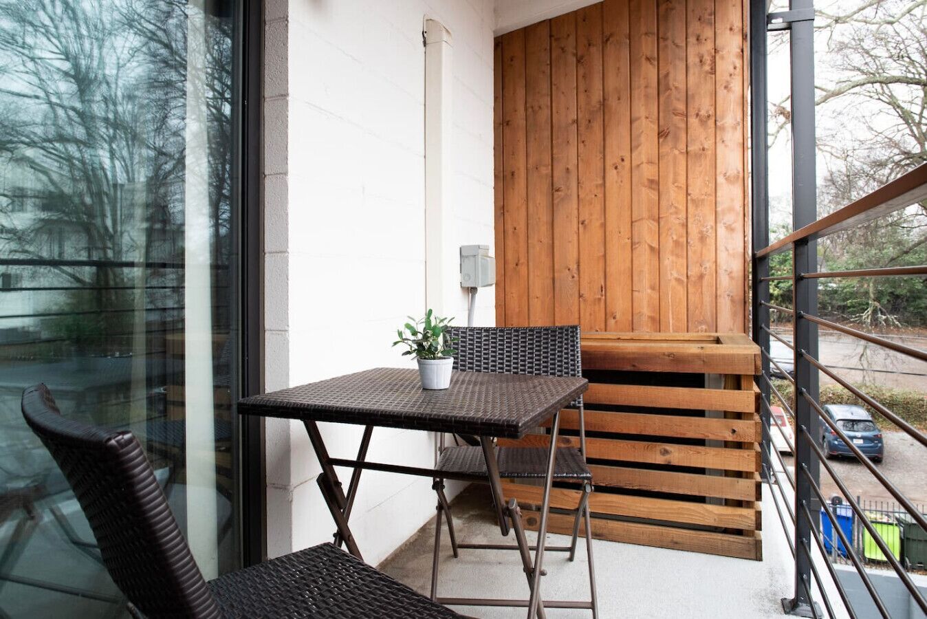 Un balcón con una mesa y sillas, una planta en maceta y un muro de madera.