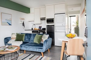 A compact living space with a blue sofa, a dining table with a bowl of fruit, and a kitchenette with a microwave, stove, and refrigerator. - The Audrey – Downtown Atlanta Apartment + Rooftop (Atlanta)