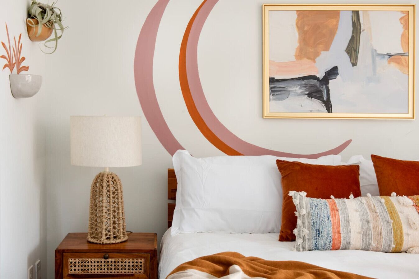 A bedroom with a bed, pillows, a bedside table with a lamp, and wall art.