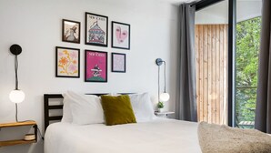 Una camera da letto con un letto, una testiera in legno, un comodino, una lampada a parete e una finestra vista verde.