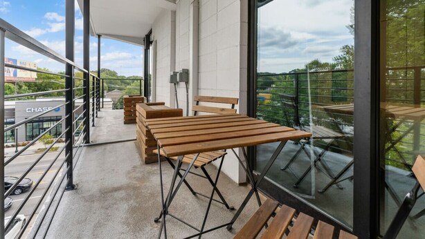Un balcone con panche in legno, un tavolo in metallo e vista sulla città.