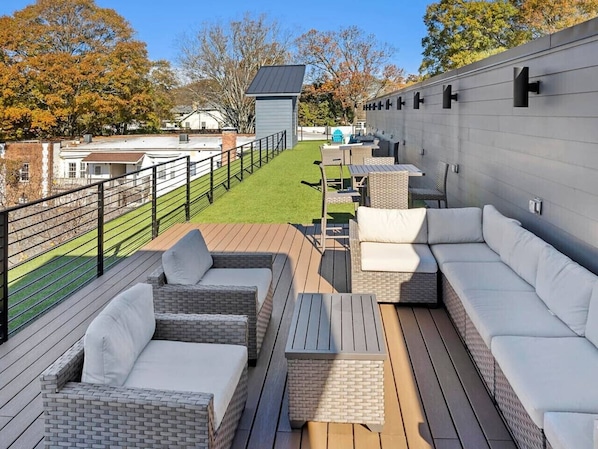 A rooftop patio with outdoor furniture, a small table, and a view of a residential area.