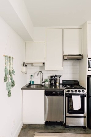 A compact kitchen with white cabinets, a stainless steel dishwasher, a gas stove, and a microwave.