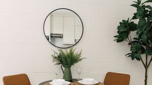 A dining area with a round table, two chairs, a mirror, a potted plant, and a small table with a vase and glasses. - LOLA > Walkable. Downtown. Rooftop. (Atlanta)