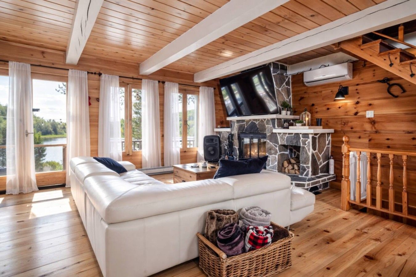 Interior acogedor de una cabaña con un sofá blanco grande, una chimenea de piedra y un televisor montado en la pared.