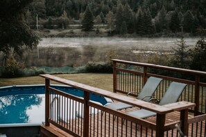 A wooden deck with a pool, surrounded by a forested area.