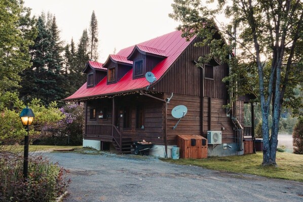A rustic wooden cabin with a red roof, a porch, and a satellite dish.