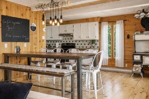 A wooden interior with a dining table, chairs, a chalkboard with messages, and a kitchen area.