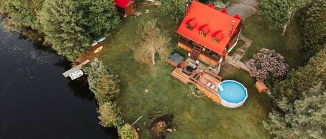 Una casa con techo rojo, piscina y muelle que se adentra en el agua.