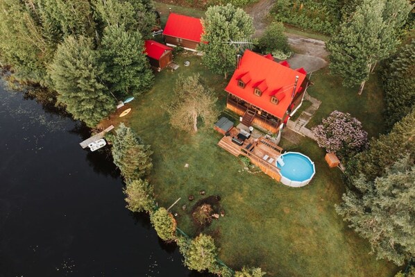 A house with a red roof, a swimming pool, and a dock extending into a body of water.