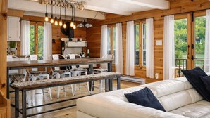 A wooden cabin interior with a dining area, white sofa, and large windows. - Le Martini Bord de l eau, spa, piscine. (Entrelacs)