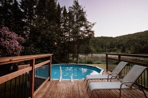 A wooden deck with a swimming pool, surrounded by trees and a view of a lake.